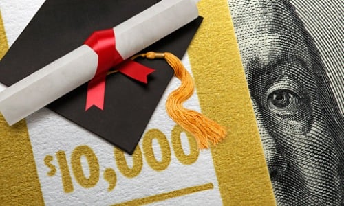 Graduation cap and a rolled-up diploma rest on top of a stack of dollar bills
