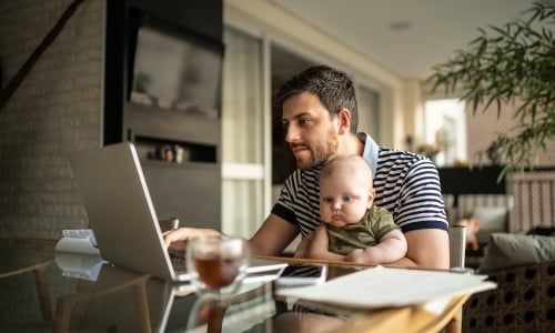 A parent using a laptop with an infant on lap