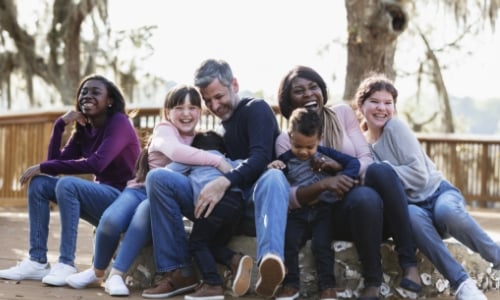 A large family sitting on a bench outside