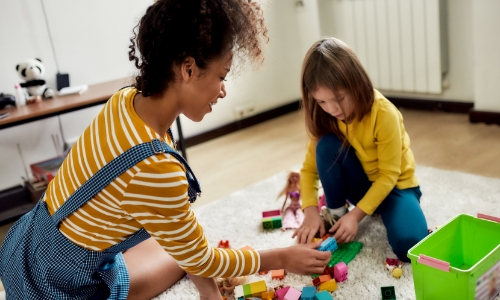 A child and babysitter playing with toys on the floor