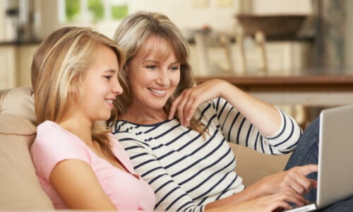 Daughter and mother smiling and looking at laptop