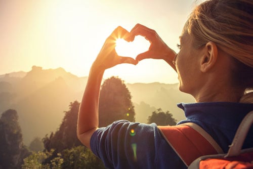 A woman is hiking and holds her hands in a heart formation