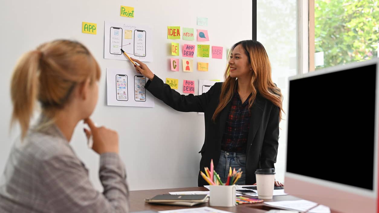 two women working in office putting design ideas on whiteboard