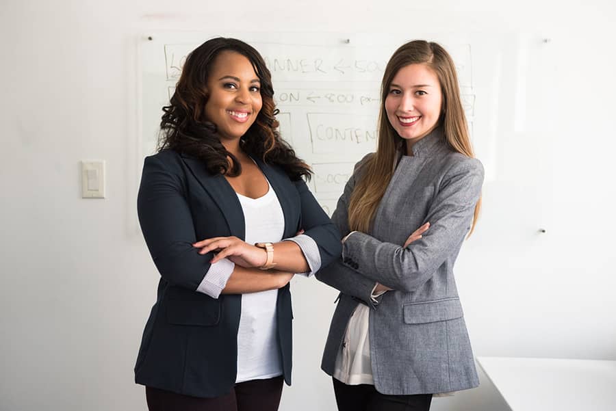 two smiling businesswomen standing in front of whiteboard