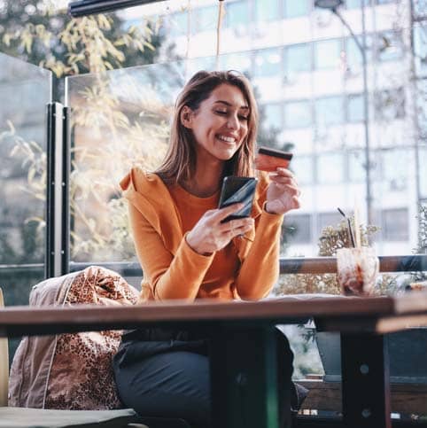 young woman sitting at a table holding phone and credit card