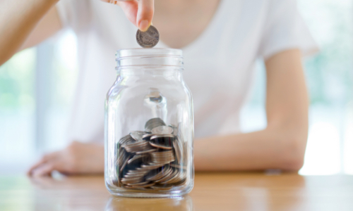 woman putting a coin into a coin jar
