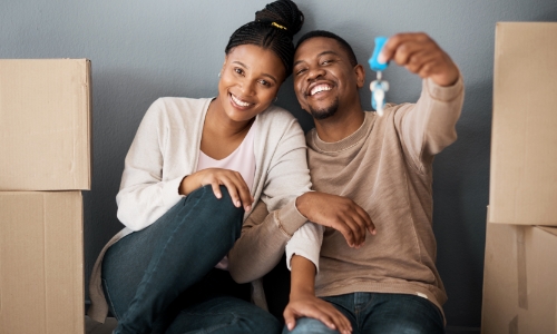 A couple sitting next to moving boxes and holding keys to their new home