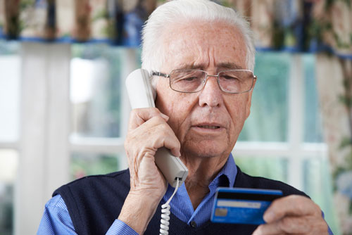 A maturely-aged man on his cellphone while holding his credit card